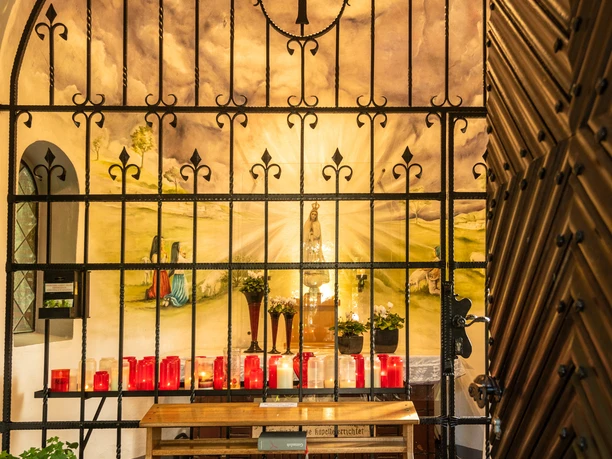 Fatimakapelle Gittertor vor Kapelle mit leuchtenden Kerzen und religiöser Wandmalerei im Hintergrund.