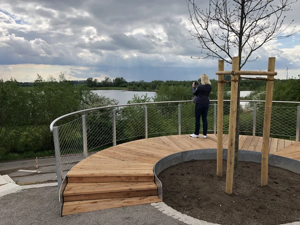 Eén persoon geniet van het weidse, bewolkte uitzicht over het platform naar een kalm meer.