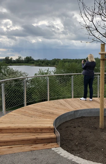 Aussichtsplattform Leese Eine Person genießt den weiten, wolkenverhangenen Blick über die Plattform auf einen ruhigen See.