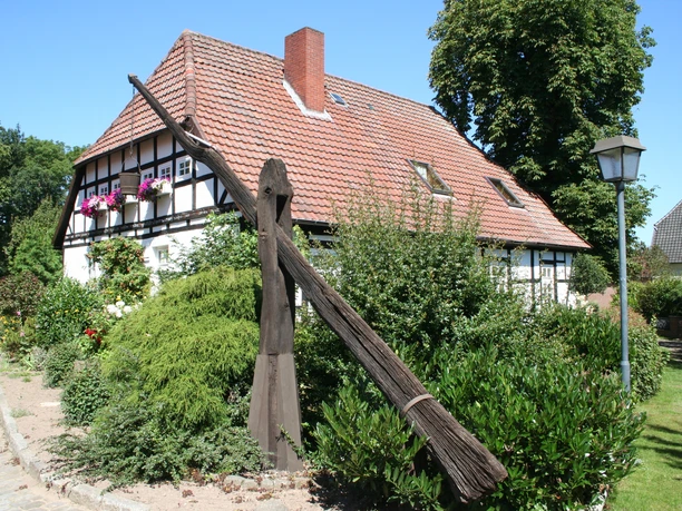 Historische put voor een vakwerkhuis met rode dakpannen en bloeiende planten.