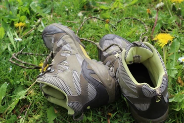 Een paar stevige wandelschoenen ligt verspreid op een bloemenweide met madeliefjes en paardenbloemen.