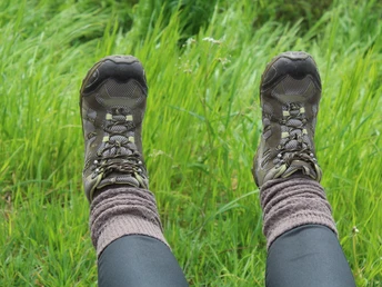 Wanderstiefel ruhen auf grünem Gras, während jemand entspannt Natur und Rasten genießt.