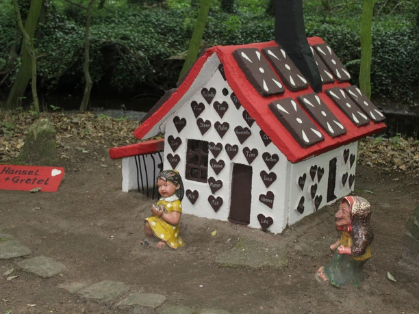 Märchenwald Pfarrbusch Steyerberg Lebkuchenhaus im Wald, umgeben von üppigem Grün, dargestellt mit Figuren von Hänsel und Gretel.