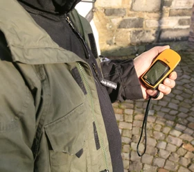 Geocaching Person hält ein GPS-Gerät in der Hand in einer historischen, gepflasterten Umgebung.