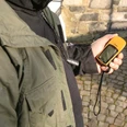 Geocaching Person hält ein GPS-Gerät in der Hand in einer historischen, gepflasterten Umgebung.