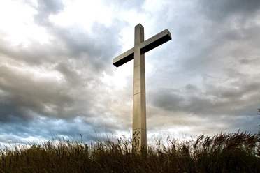 Barbarakreuz Ein großes Kreuz ragt majestätisch gegen einen dramatisch bewölkten Himmel hervor, umgeben von Gras.