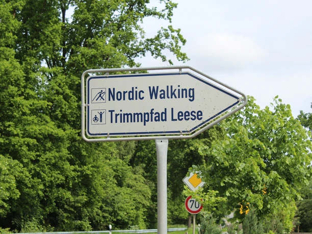 Bord dat naar Nordic Walking- en fitnessroute Leese wijst, omgeven door groene bomen, vlakbij landweg.