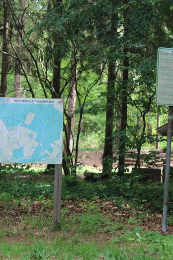 Ein Infoboard und ein Schild in einem Wald zeigen den Beginn des Nordic Walking und Trimpfads Leese.