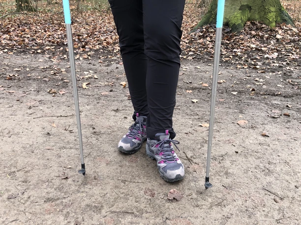 Person Nordic walking on a leaf-lined forest path, equipped with poles and running shoes.