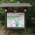 Eine Informationstafel mit Übersichtsplan und Sponsorlogos steht in einem grünen Waldgebiet.