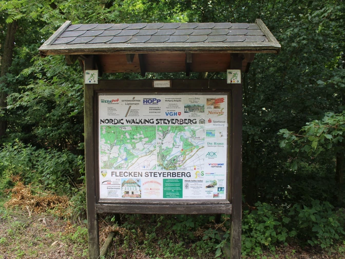 Eine Informationstafel mit Übersichtsplan und Sponsorlogos steht in einem grünen Waldgebiet.