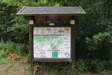 Nordic Walking Steyerberg Eine Informationstafel mit Übersichtsplan und Sponsorlogos steht in einem grünen Waldgebiet.