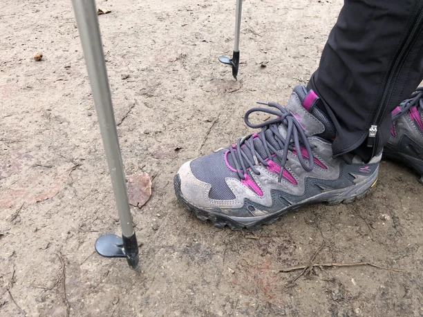 Nordic Walking Ein Wanderschuh tritt mit zwei Nordic Walking-Stöcken auf einem unbefestigten Waldweg auf.