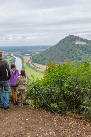 Aussicht Porta Kanzel auf das Kaiser Wilhelm Denkmal Familie betrachtet das Kaiser Wilhelm Denkmal auf bewaldetem Hügel, umgeben von einer weitläufigen Landschaft.