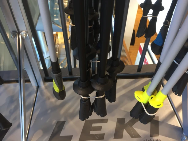 Nordic walking poles of different colors and models hanging on a stand in a store.