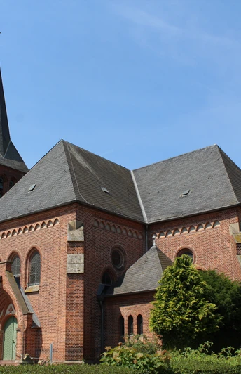 Alte Backsteinkirche mit markantem Turm in ländlicher Umgebung, blauer Himmel im Hintergrund.