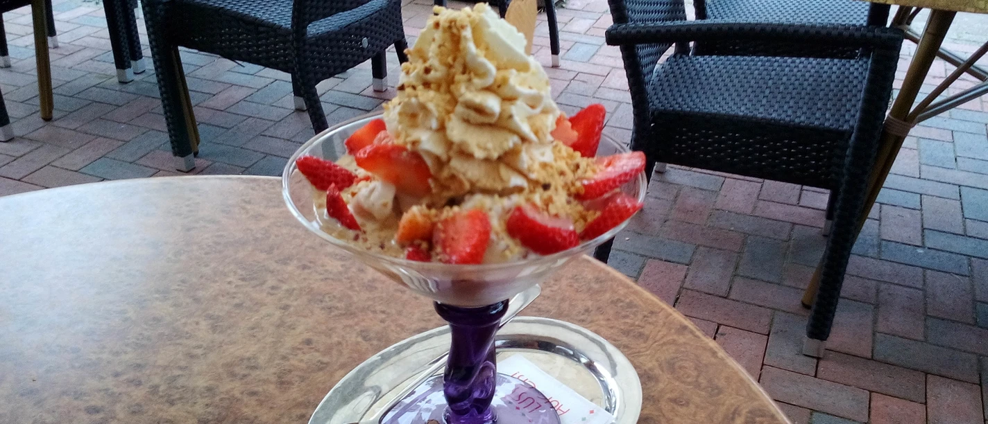 Strawberry sundae with cream and nuts on a terrace with paving stones and garden furniture.