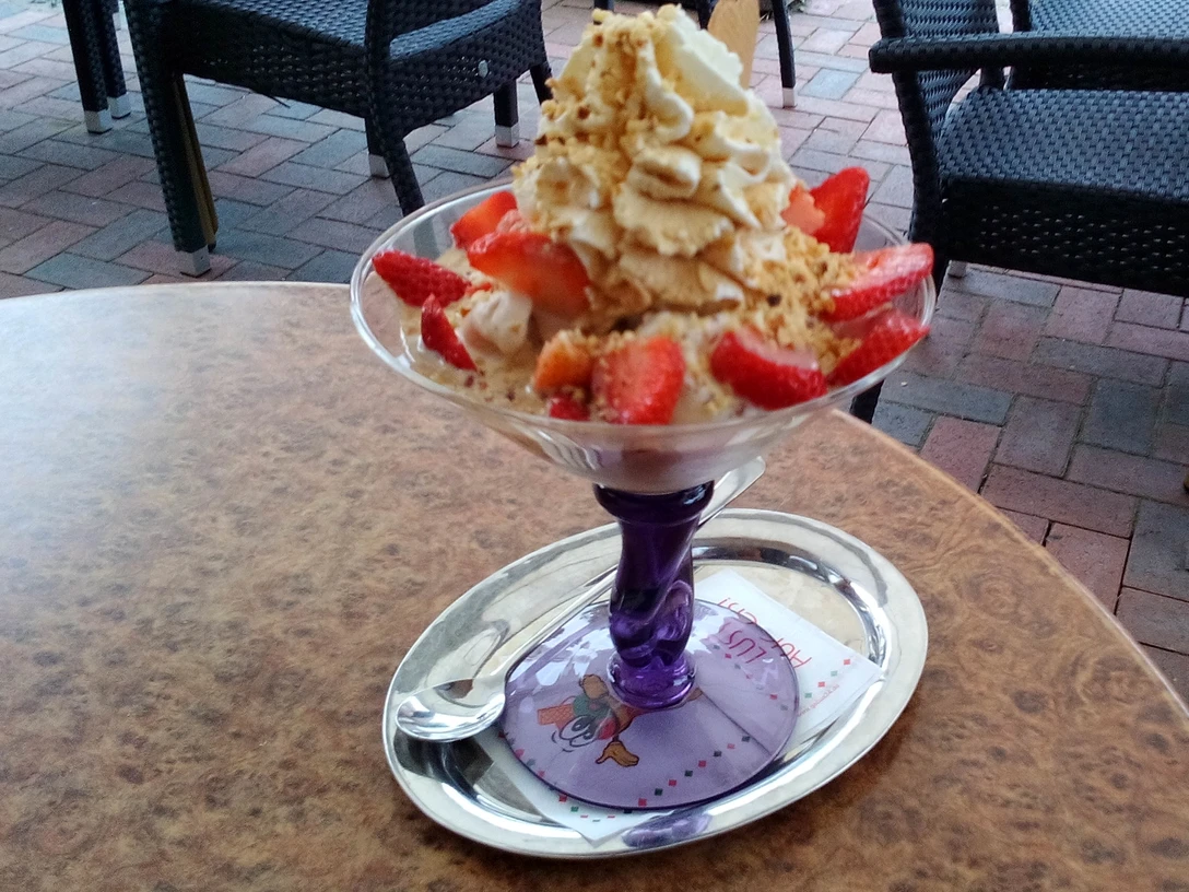 Erdbeer Eisbecher Erdbeer Eisbecher mit Sahne und Nüssen auf einer Terrasse mit Pflastersteinen und Gartenmöbeln.Strawberry sundae with cream and nuts on a terrace with paving stones and garden furniture.Jordbæris med fløde og nødder på en terrasse med belægningssten og havemøbler.Aardbeienijs met slagroom en noten op een terras met stoeptegels en tuinmeubilair.