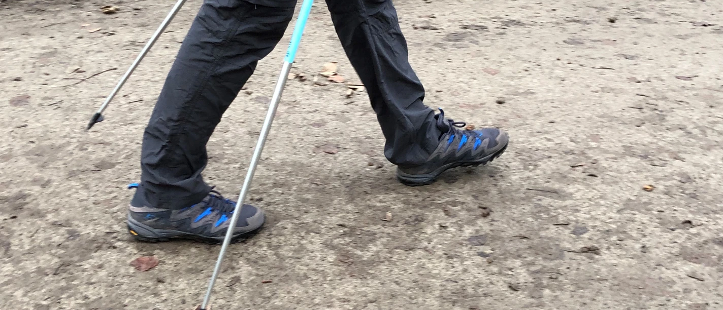 Person on forest path Nordic walking with poles, autumn ground, focus on legs and shoes.
