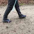 Nordic Walking Person auf Waldweg beim Nordic Walking mit Stöcken, herbstlicher Boden, Fokus auf Beine und Schuhe.