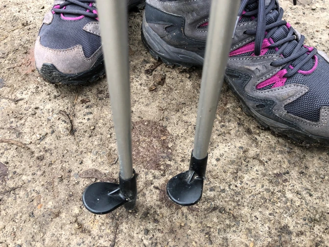 Wanderschuhe und Nordic Walking-Stöcke auf einem Betonweg, bereit für Outdoor-Aktivitäten.