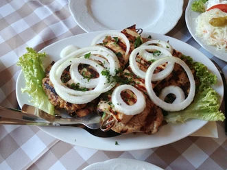 Grillfleischspieße mit Zwiebelringen und frischen Kräutern auf einem Teller mit Salatgarnitur.