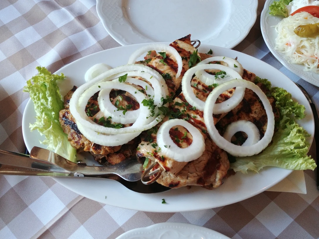 Griechisches Gericht Grillfleischspieße mit Zwiebelringen und frischen Kräutern auf einem Teller mit Salatgarnitur.