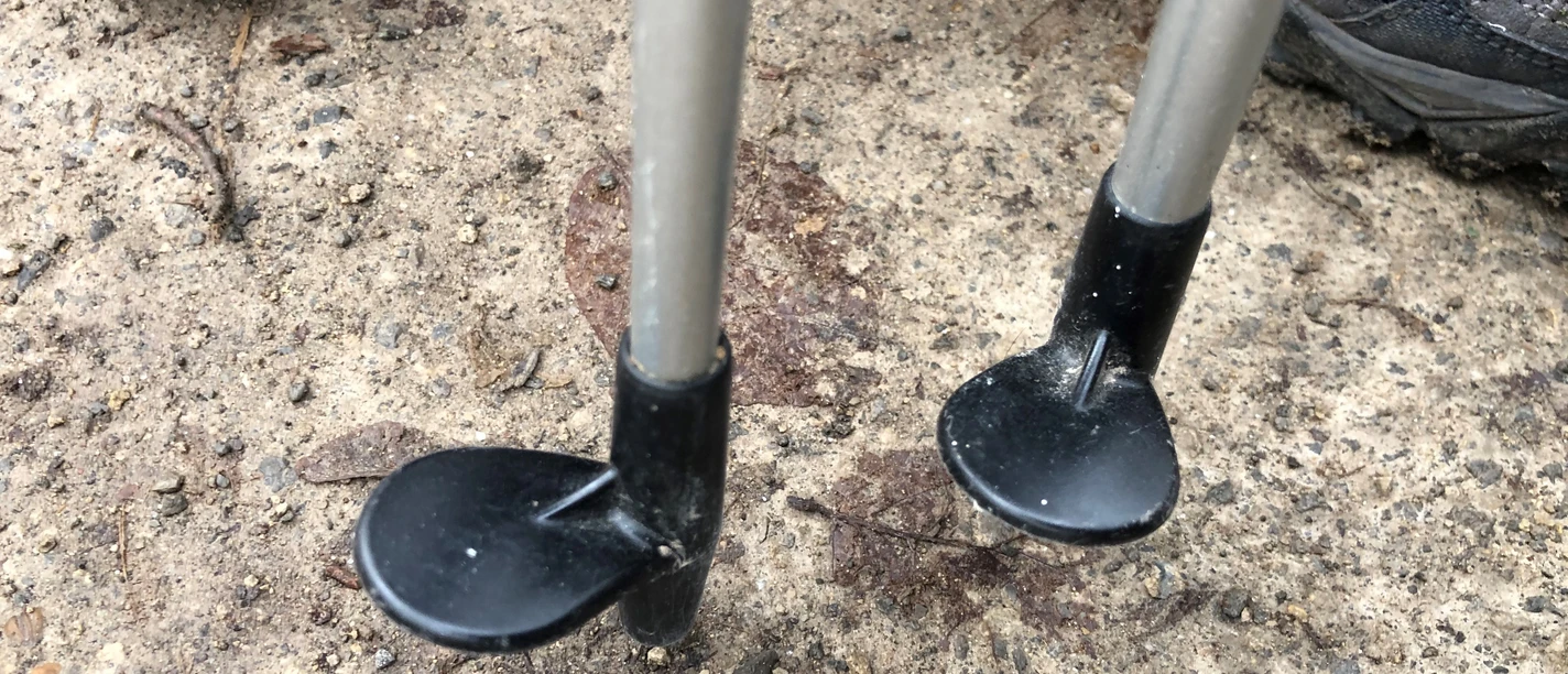 Two Nordic walking poles stand on a parquet-like path, surrounded by sports shoes.