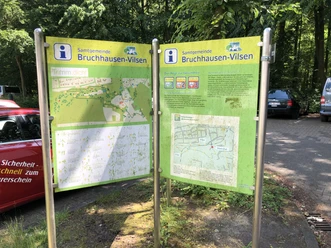 Terrainkurwege Bruchhausen-Vilsen Zwei Infotafeln in Bruchhausen-Vilsen mit Wanderkarten stehen auf einem befestigten Parkplatz im Grünen.