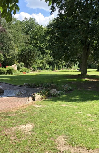 Kurpark Bruchhausen-Vilsen mit Springbrunnen, gepflegten Rasenflächen und schattenspendenden Bäumen.