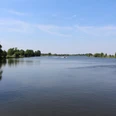 Dörverden Weser Weitläufige Flusslandschaft mit Bäumen unter blauem Himmel, ruhiges Wasser, Boote in der Ferne.