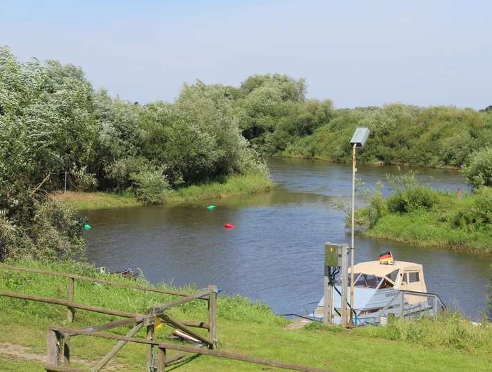 Ein Flussabschnitt mit einem Boot am Ufer, umgeben von grüner Vegetation und einem blauen Himmel.