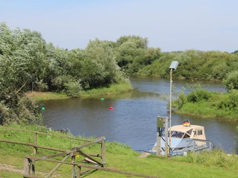 Aller bei Westen Ein Flussabschnitt mit einem Boot am Ufer, umgeben von grüner Vegetation und einem blauen Himmel.