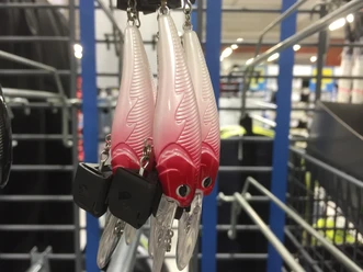Angelhaken Drei kunstvolle Angelköder in rot-weiß mit Federmuster hängen an einer Metallhalterung in einem Geschäft.