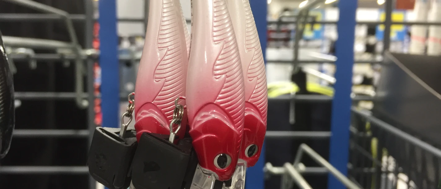 Angelhaken Drei kunstvolle Angelköder in rot-weiß mit Federmuster hängen an einer Metallhalterung in einem Geschäft.