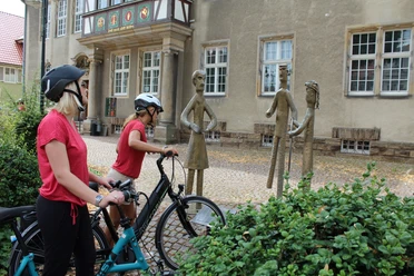 Familienskulptur Petershagen Zwei Radfahrer betrachten eine metallerne Skulpturengruppe in einer historischen Altstadt.