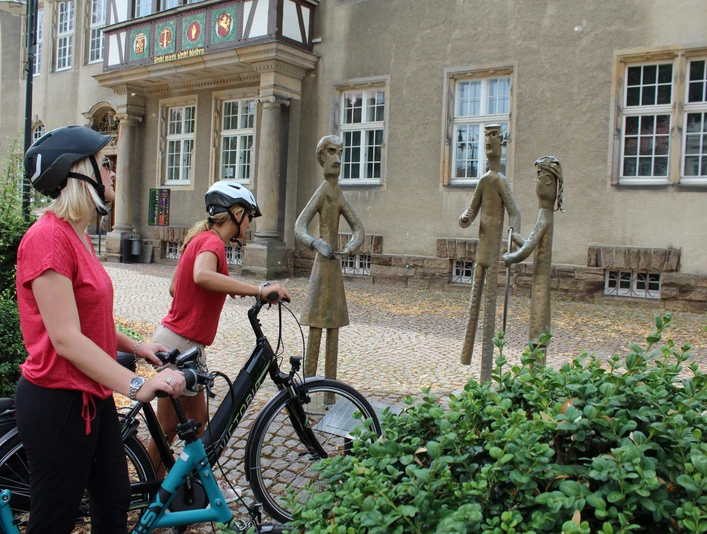 Familienskulptur Petershagen Zwei Radfahrer betrachten eine metallerne Skulpturengruppe in einer historischen Altstadt.