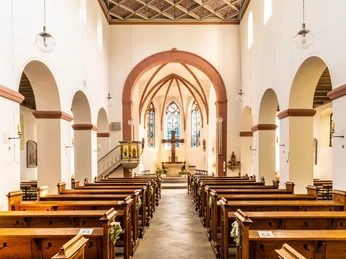 Innenstadt <p>Innenansicht einer Kirche mit Holzbänken und buntem Glasfenster im Hintergrund.</p>