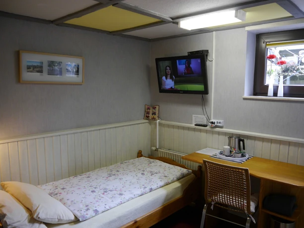 Ein Einzelzimmer mit Bett, Holztisch, Stuhl und Wand-TV, dekoriert mit Bildern und Blumenvase.