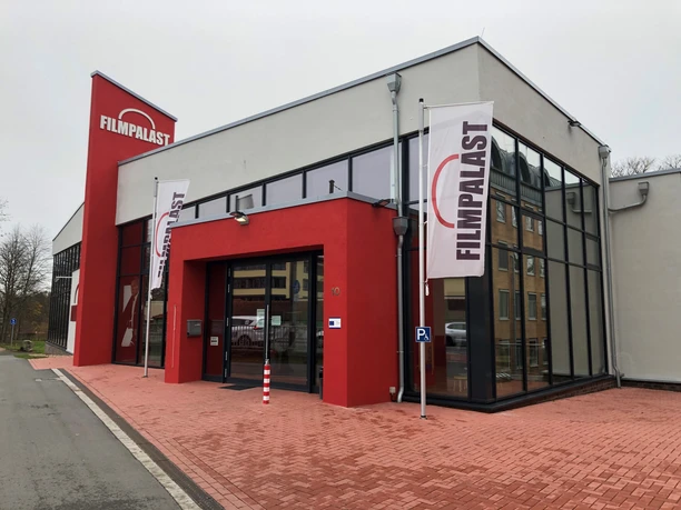 Rotes Gebäude mit großen Fenstern und Filmpalast-Schriftzügen, zwei Flaggen wehen davor.