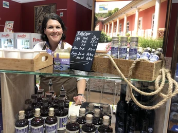 Frau hinter einem Stand bietet verschiedene Liköre und Honig in einer rustikalen Umgebung an.