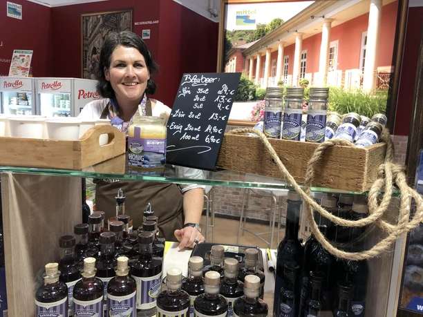 Früchtehof Schindler Frau hinter einem Stand bietet verschiedene Liköre und Honig in einer rustikalen Umgebung an.