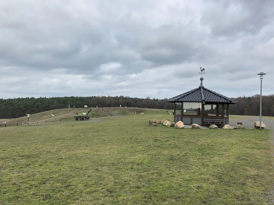 Weites, grünes Plateau mit einer kleinen, überdachten Holzhütte, umgeben von sanften Hügeln.
