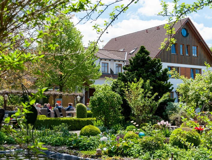 Üppige Gartenlandschaft mit blühenden Sträuchern umrahmt ein traditionelles Landhaus mit roten Ziegeldach.