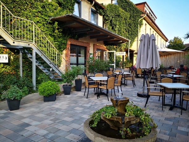 Well-kept outdoor terrace of an inn with elegant tables, embraced by lush green ivy.