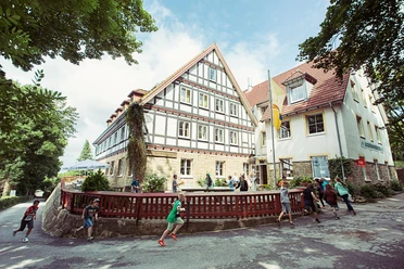 DJH Jugendherberge Tecklenburg - Außenansicht Kinder laufen vor der historischen Fassade der DJH Jugendherberge Tecklenburg. Luftige Baumkronen umrahmen die Szene.