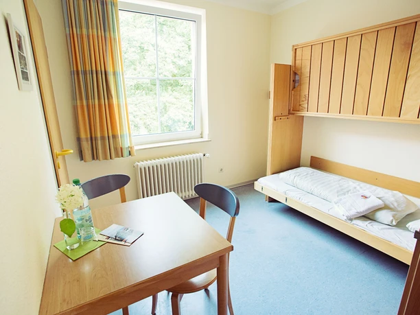 DJH Jugendherberge Tecklenburg - Zimmer Ein einfach eingerichtetes, helles Zimmer mit Holzmöbeln, einem Fenster und einem Ausblick auf grüne Natur.