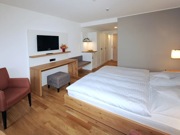 Landhotel Annelie - DZ Komfort Ein modernes Doppelzimmer mit Holzfußboden, gemütlichem Bett, Flachbild-TV und Sessel.