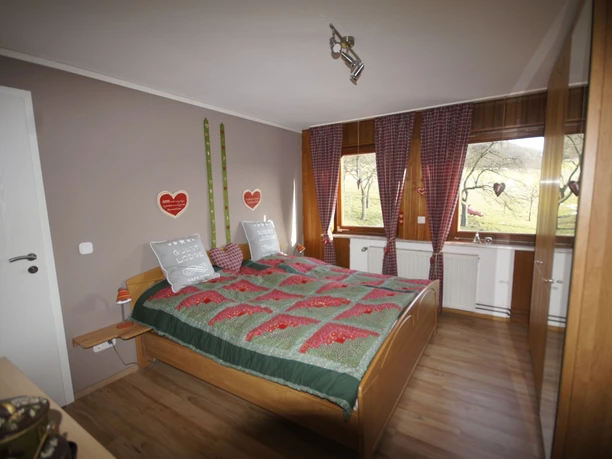 Schlafzimmer mit Doppelbett Doppelbett in warm dekoriertem Raum mit Holzfußboden, Fenster mit Blick ins Grüne, herzförmige Details.