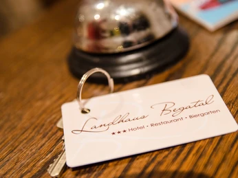 Rezeption Schlüsselkarte mit Landhaus-Logo auf hölzerner Rezeption, daneben eine glänzende Silberklingel.